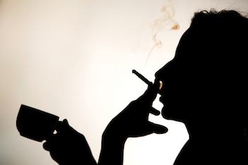 Silhouette of person smoking a cigarette and holding a cup of coffee.