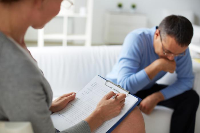 Man receiving therapy from a therapist with clipboard.